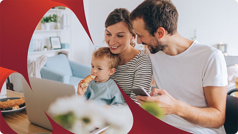 A family is gathered around a table in a cozy, modern living space. The scene includes a laptop, some pastries on plates, and a smartphone.