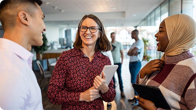 Three people standing indoors talking to each other and smiling.