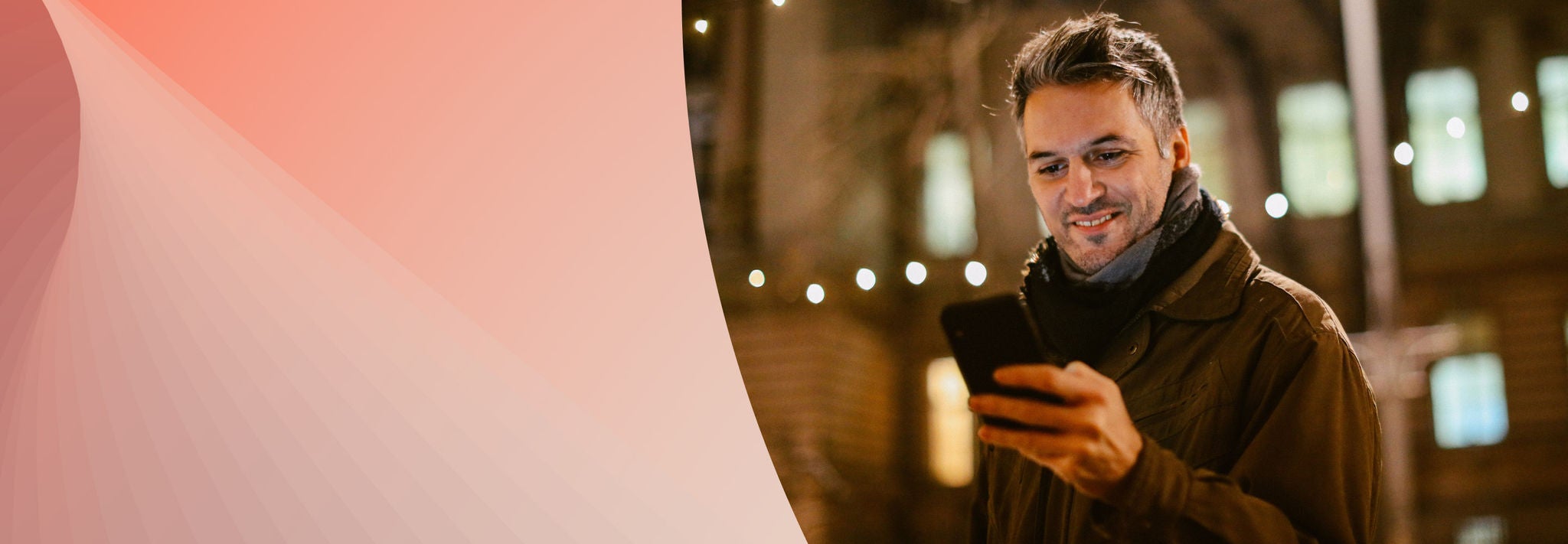 Person in winter clothing outdoors at night looking at a cellphone.