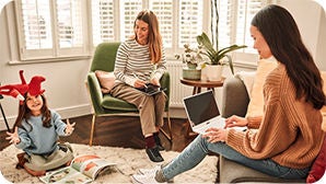 Two women working from home in a living room as a young child is playing with a stuffed animal.