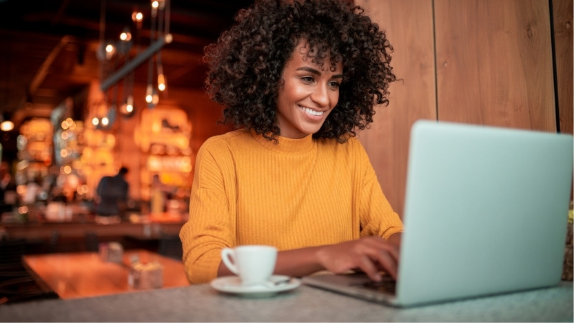 A young woman works on her laptop, smiling as she is typing on her laptop's keyboard.