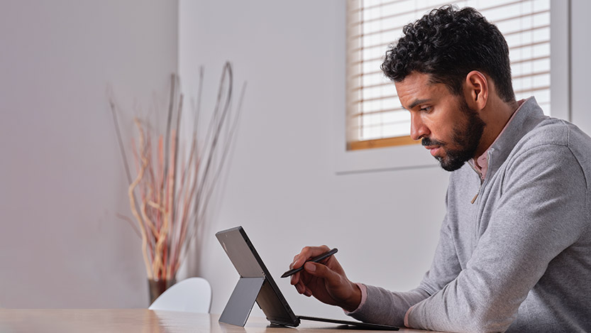 A man indoors works on a tablet with a stylus.