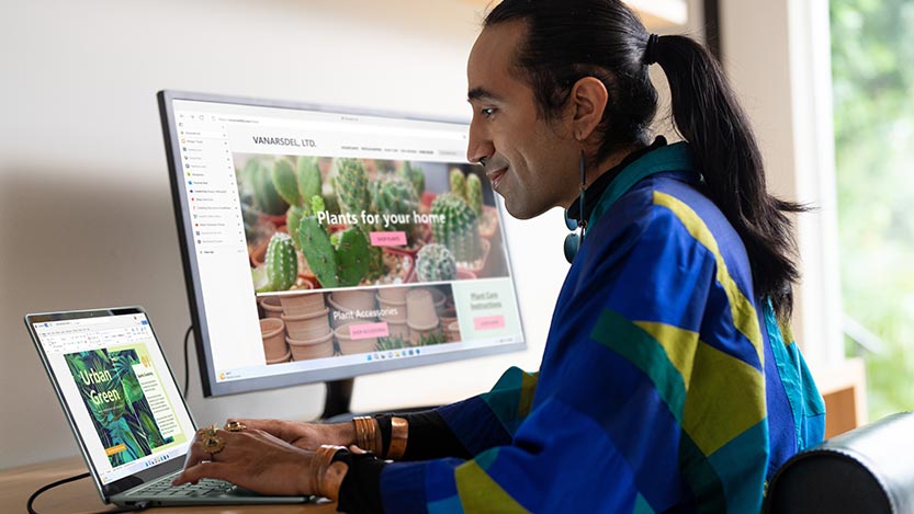 A man sitting at a desk works on a laptop computer and a monitor