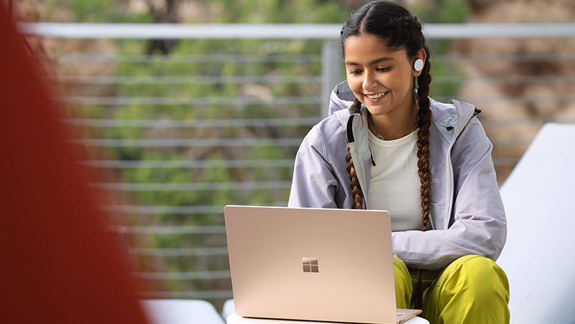 A young woman sitting outside smiles while working on her computer.