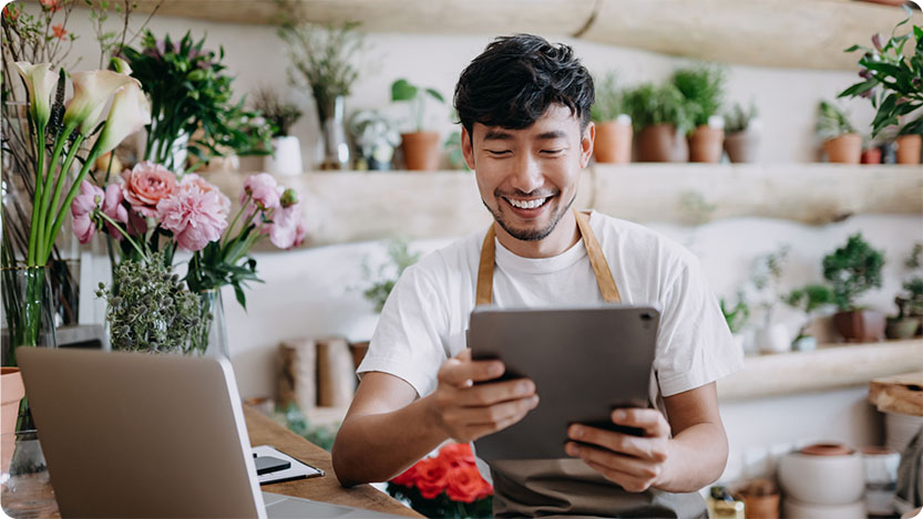 A person sitting by a desk holding a tablet and smiling