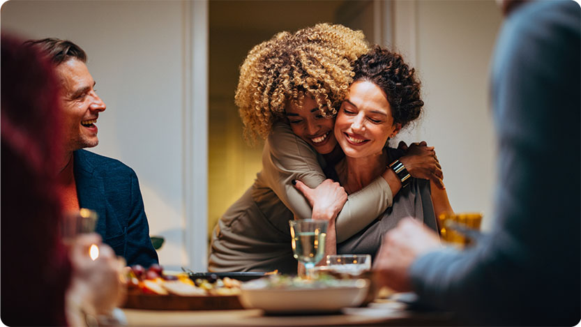 People having dinner, two of them are hugging and smiling.