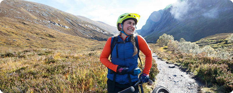 Happy biker smiling while holding a bike in a mountain setting.