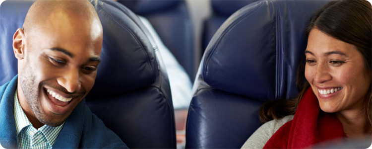 Two smiling people sitting next to each other on an airplane.