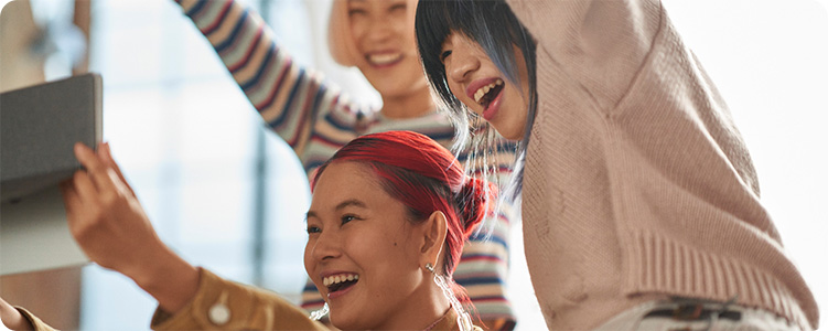 Three happy people smiling and laughing while holding a tablet.